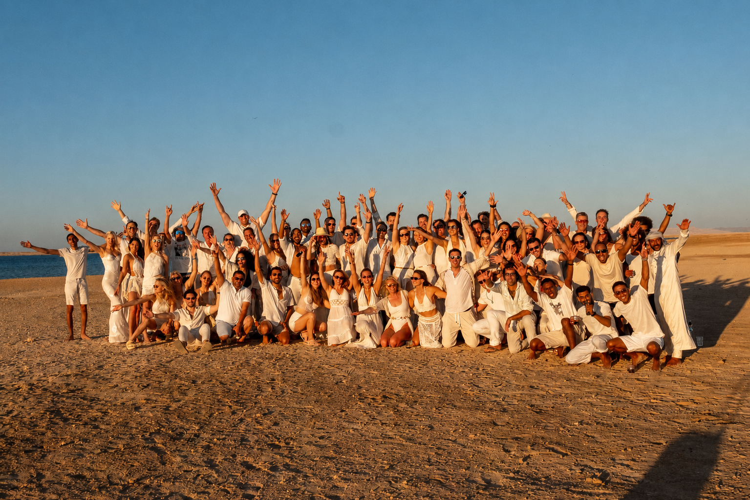 The whole crew in white celebrating together on the beach at sunset