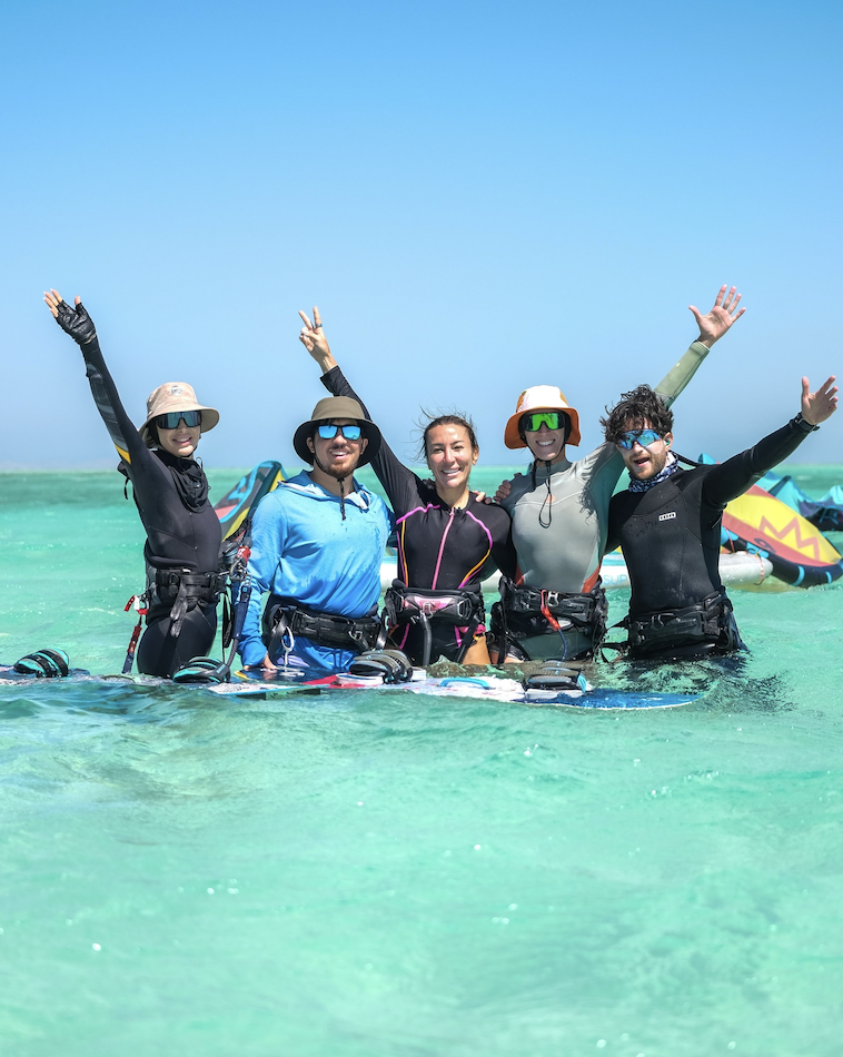 Group of friends in kitesurfing gear celebrating in turquoise water